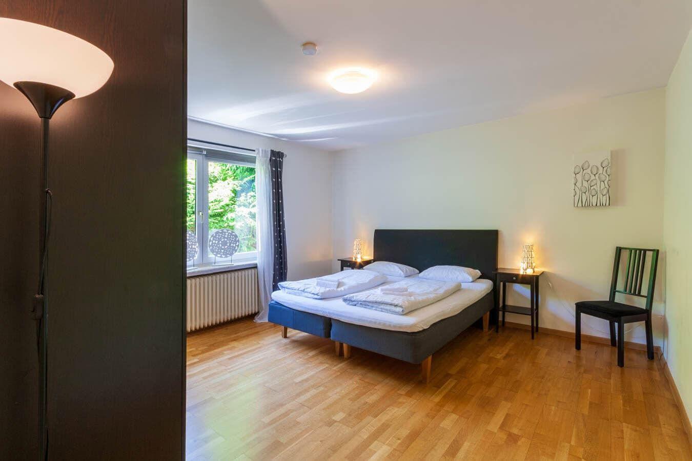 Schlafzimmer mit Doppelbett, Holzboden und Fenster mit Blick auf Grün.