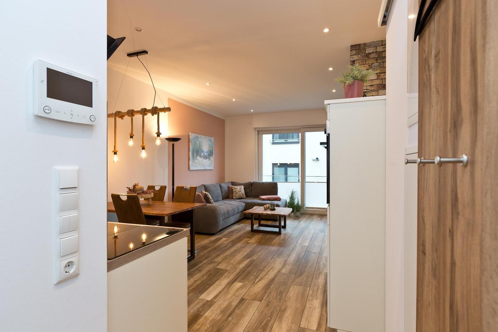 Wohnbereich mit Sofa, Tisch und Holzboden. Küche mit Thermostat und Lichtschalter.