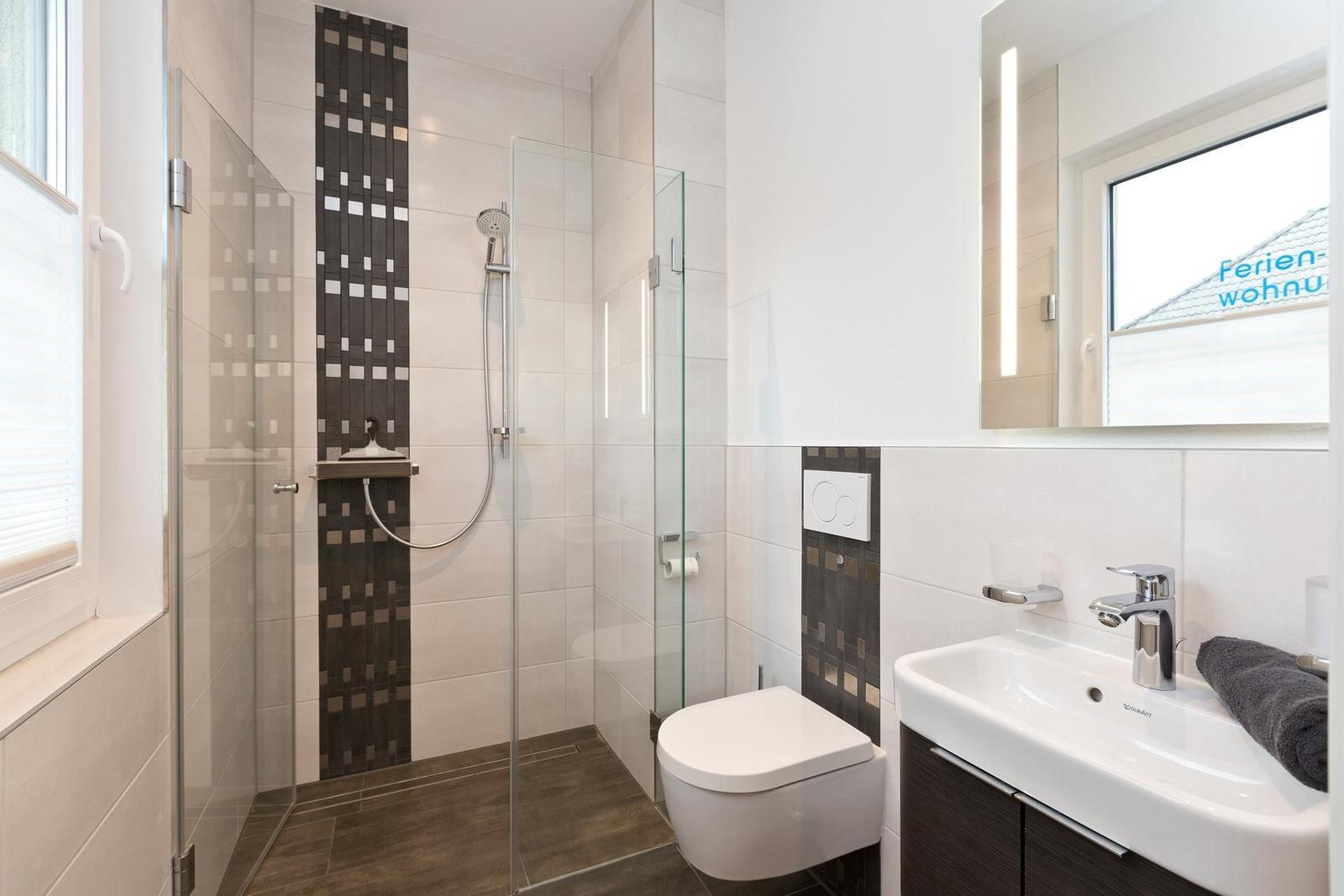 Duschbereich mit Glaswand, Toilette und Waschbecken mit Spiegel.