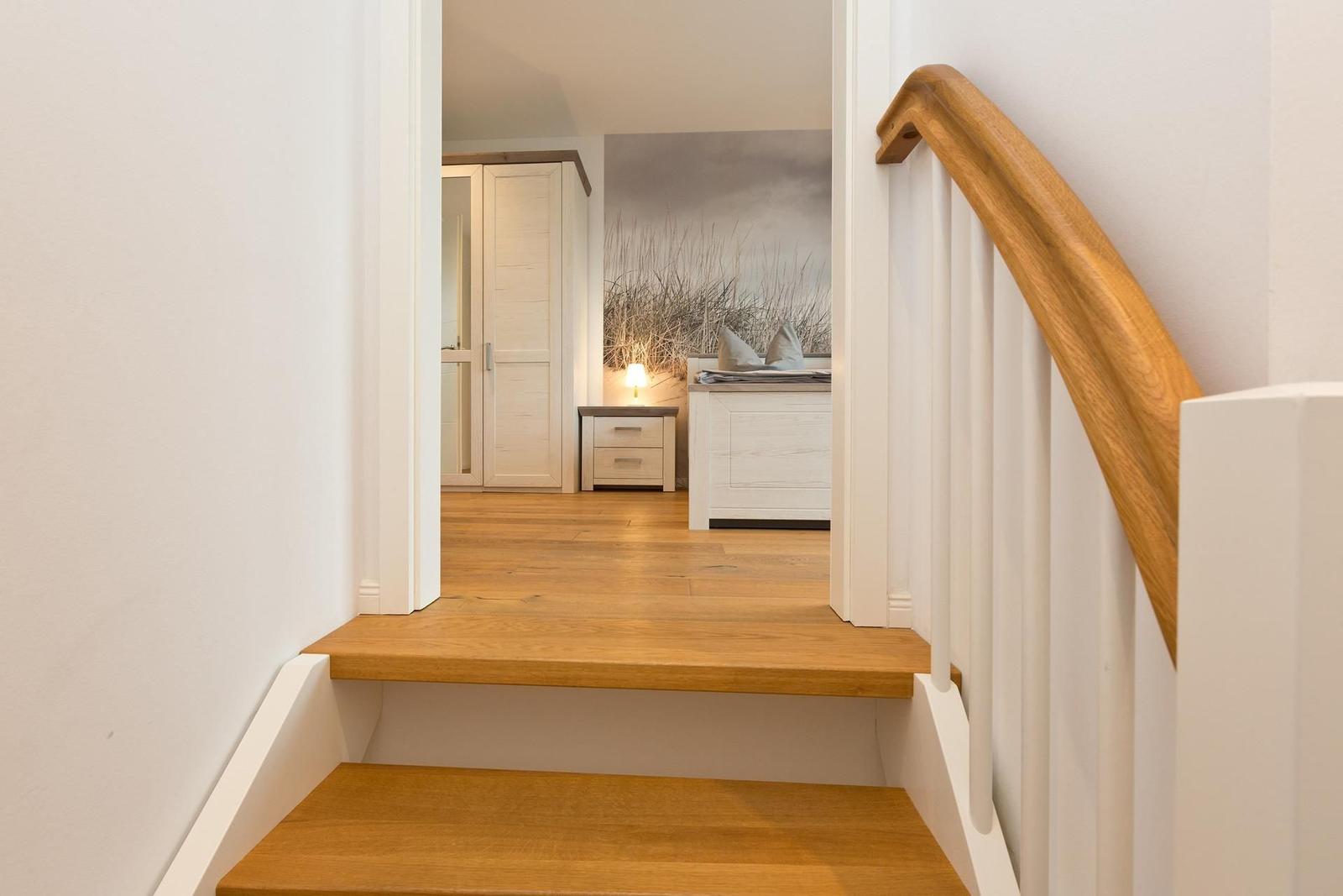 Treppenhaus mit Holzstufen und weißer Balustrade führt in ein Schlafzimmer mit Bett und Kleiderschrank.