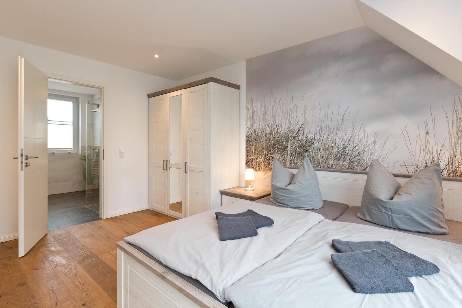 Schlafzimmer mit Dachschrägen, Bett, Kleiderschrank und Blick in die Dusche.