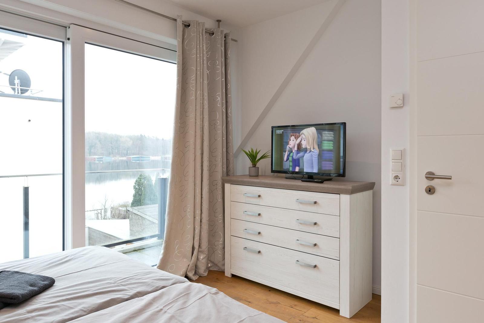 Schlafzimmer mit TV, Balkon und Blick auf den See.