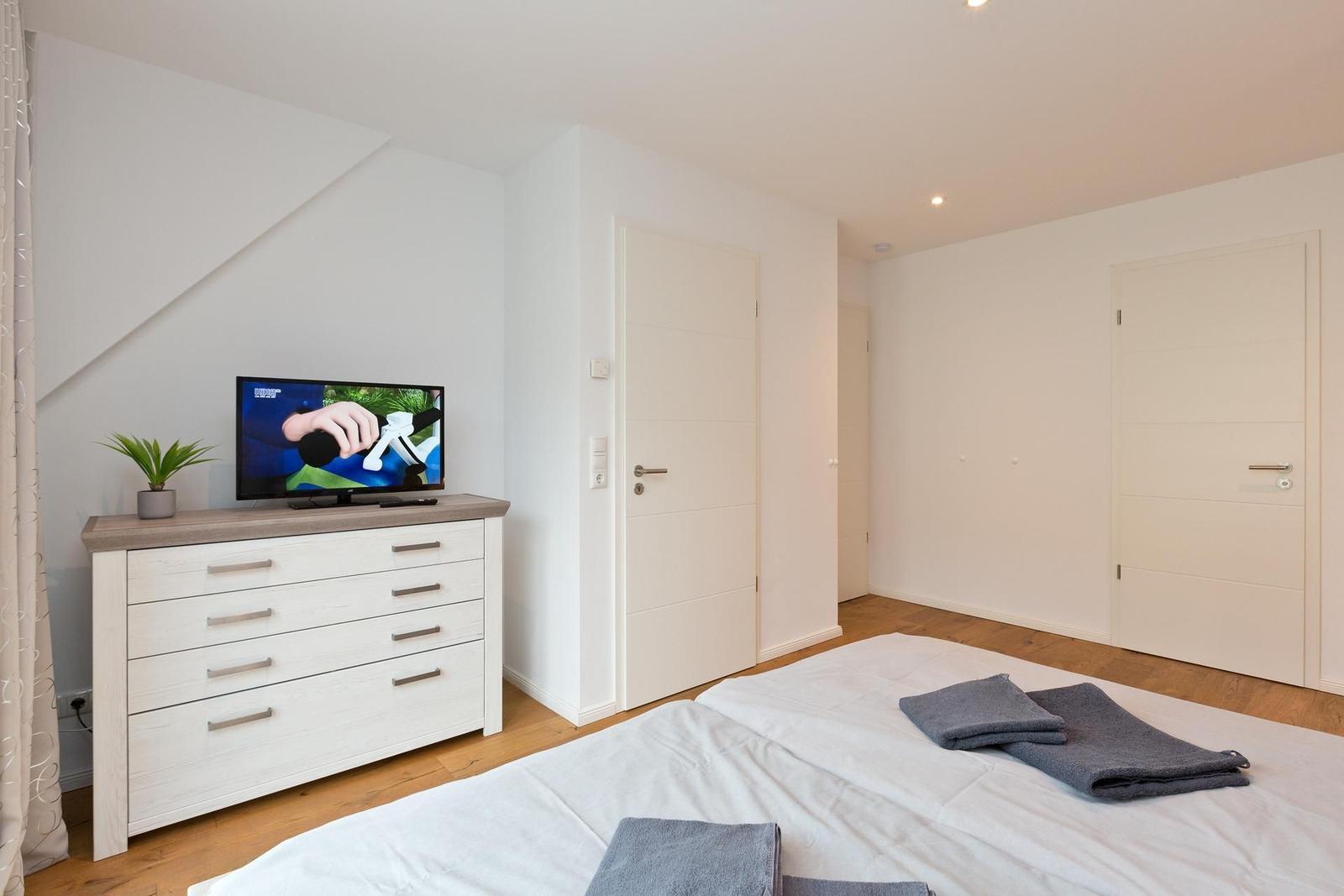 Schlafzimmer mit Bett, TV und Schrank. Holzboden und weiße Wände.