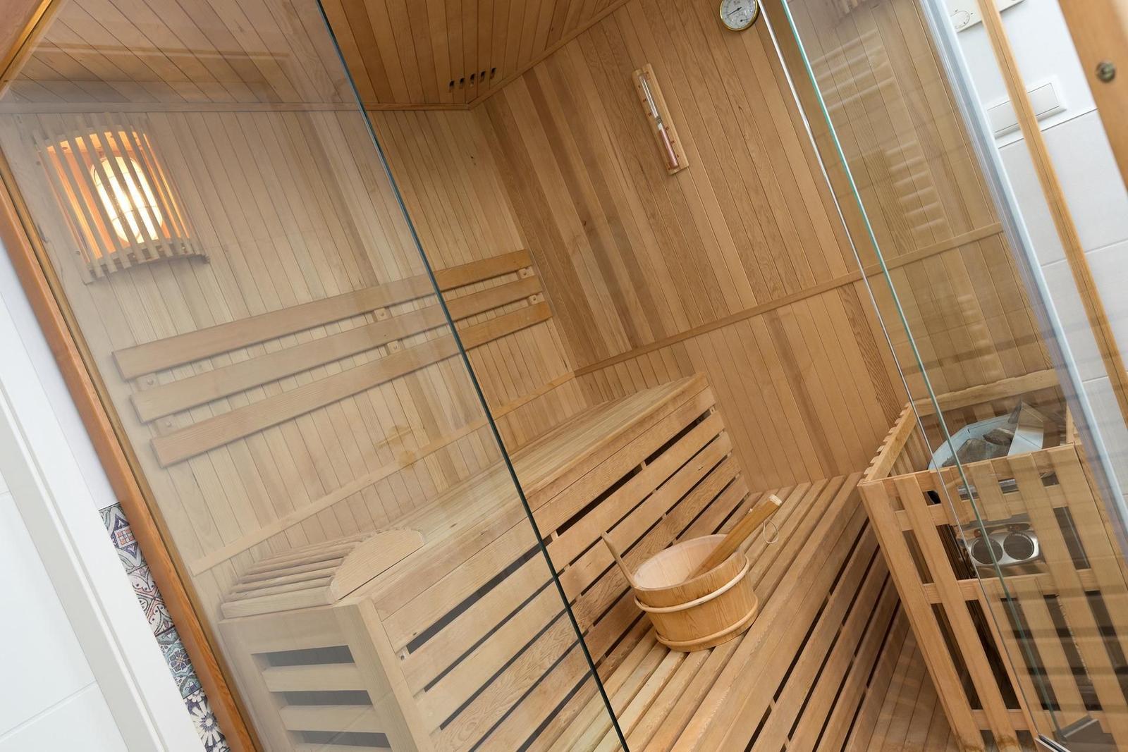 Sauna mit Holzbank, Holzschale und Glaswand.