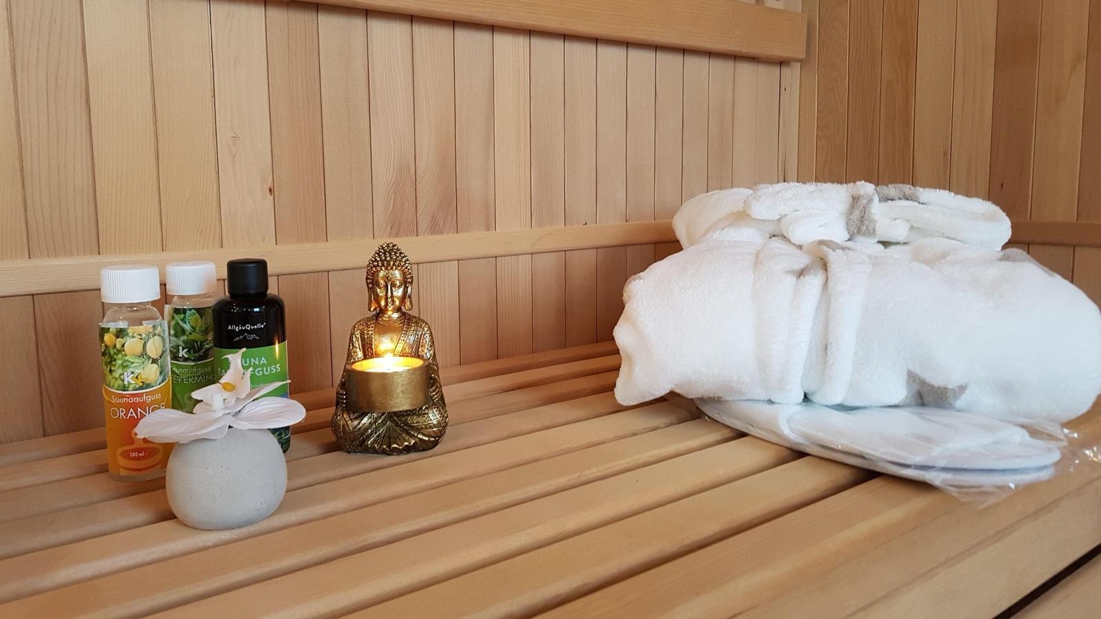 Sauna mit Holzbank, gefaltetem Handtuch, Duftölen und brennender Buddha-Lampe.