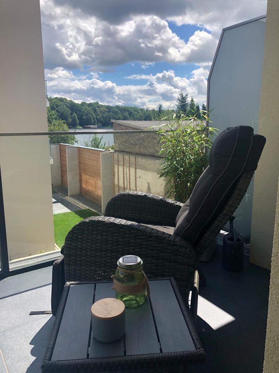 Terrasse mit Liegestuhl und Tisch. Blick auf Wasser und Bäume.
