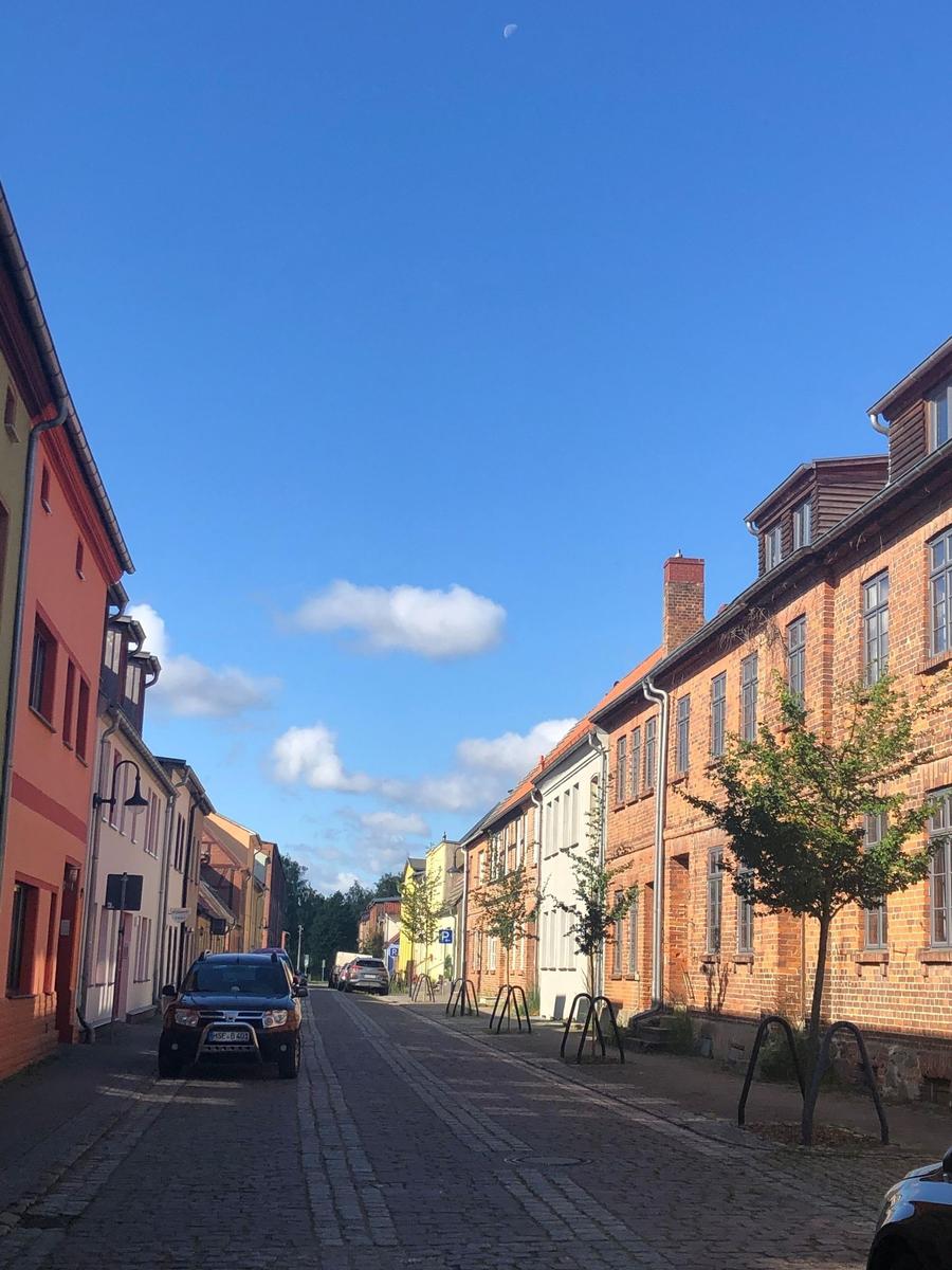 Enge Straße mit historischen Gebäuden und gepflastertem Boden unter blauem Himmel.