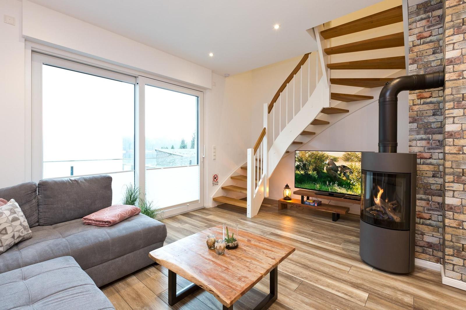 Wohnzimmer mit Sofa, Kamin, Fernseher und Holztreppe.