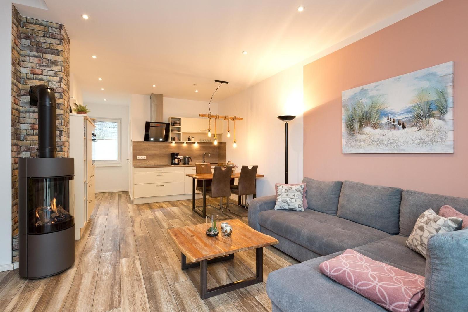 Wohnzimmer mit Sofa, Kamin und offener Küche im Hintergrund.