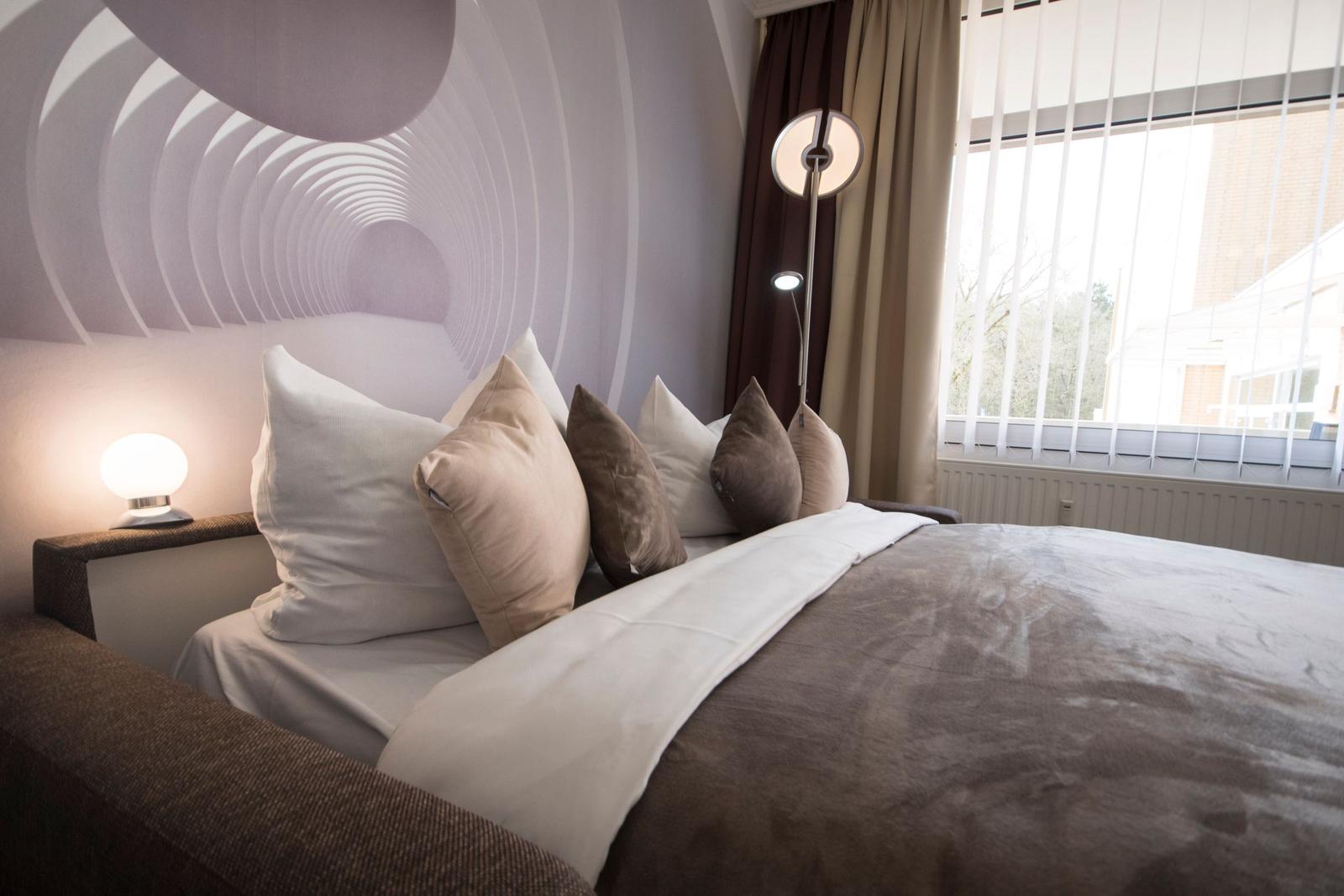 Ein Bett mit Kissen und Decke vor einem Fenster mit Jalousien und einer Wanddekoration.