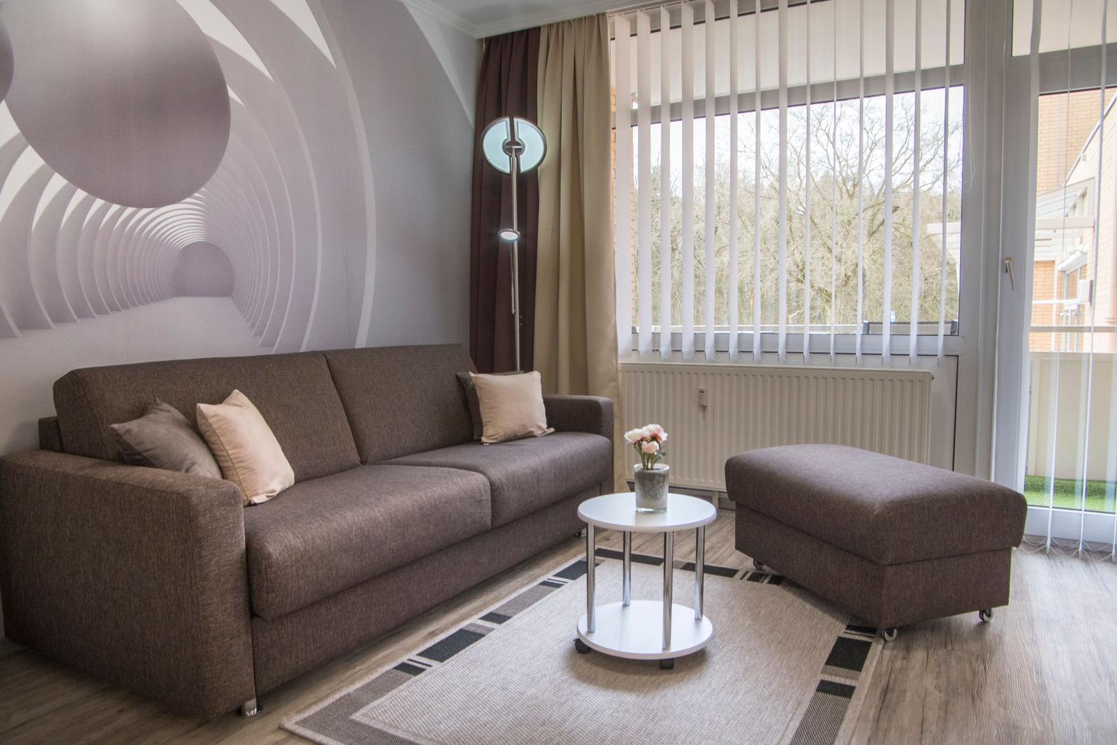Wohnzimmer mit Sofa, Sitzbank und Tisch vor großem Fenster.