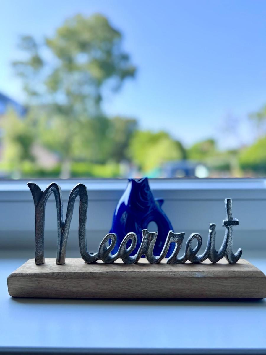 Metall-Schild mit Meerrett auf Holzsockel, blauer Glasfigur im Hintergrund.