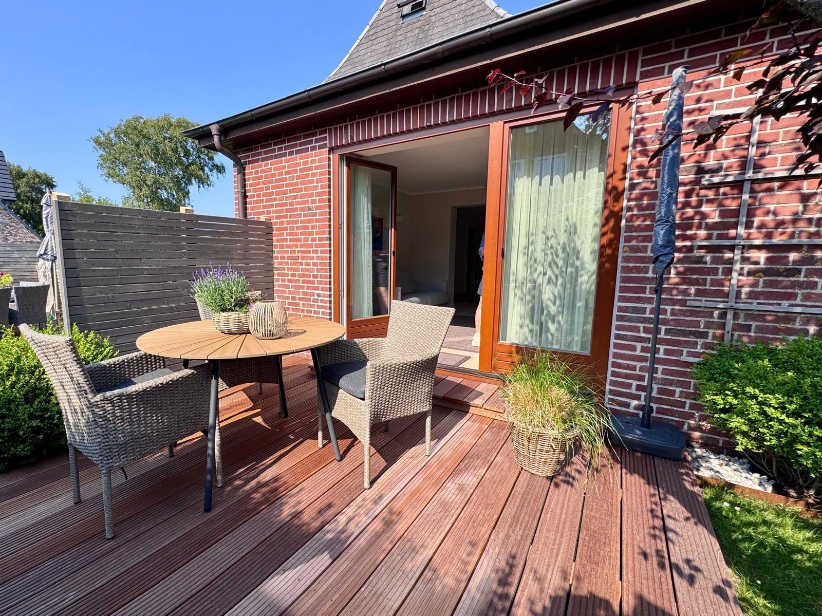 Terrasse mit Holztisch, Stühlen und Pflanzen. Durchgang zur Wohnung. Roter Backsteinbau.