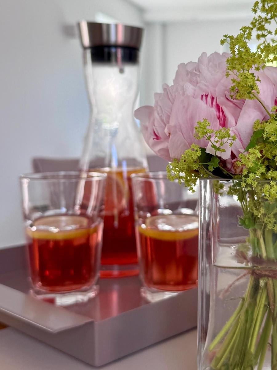 Auf einem Tablett stehen zwei Gläser mit Getränk und eine Karaffe. Rechts steht eine Vase mit Blumen.