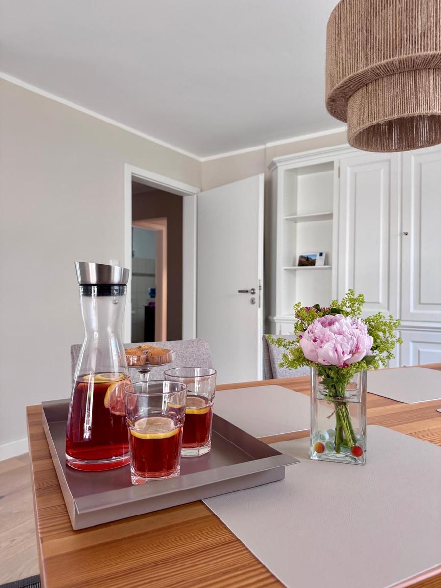 Esstisch mit Serviertray, Blumen und Getränken. Hintergrund: weiße Schränke und Tür.