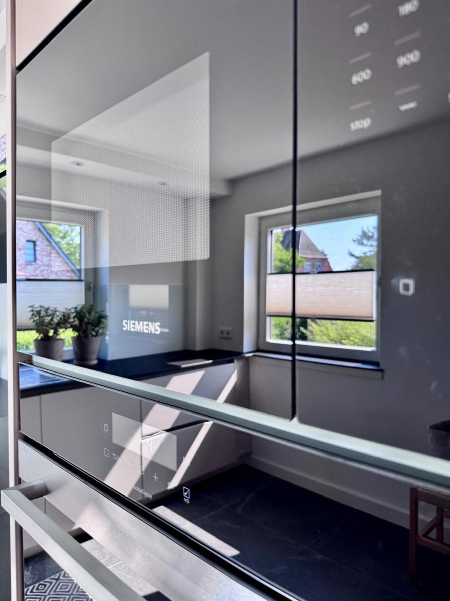 Moderne Küche mit Glasfront und integriertem Ofen. Fenster zeigt Außenbereich.