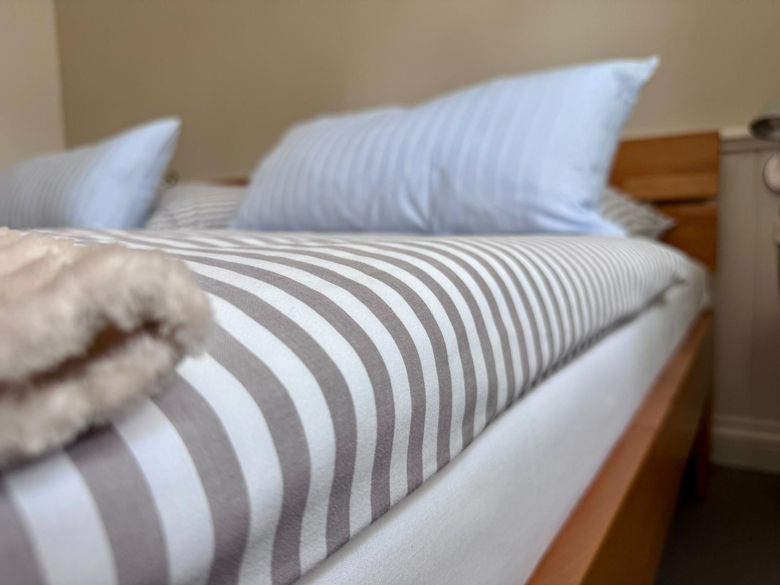 Ein Bett mit gestreifter Bettwäsche und Kissen. Holzrahmen und gefaltete Decke.