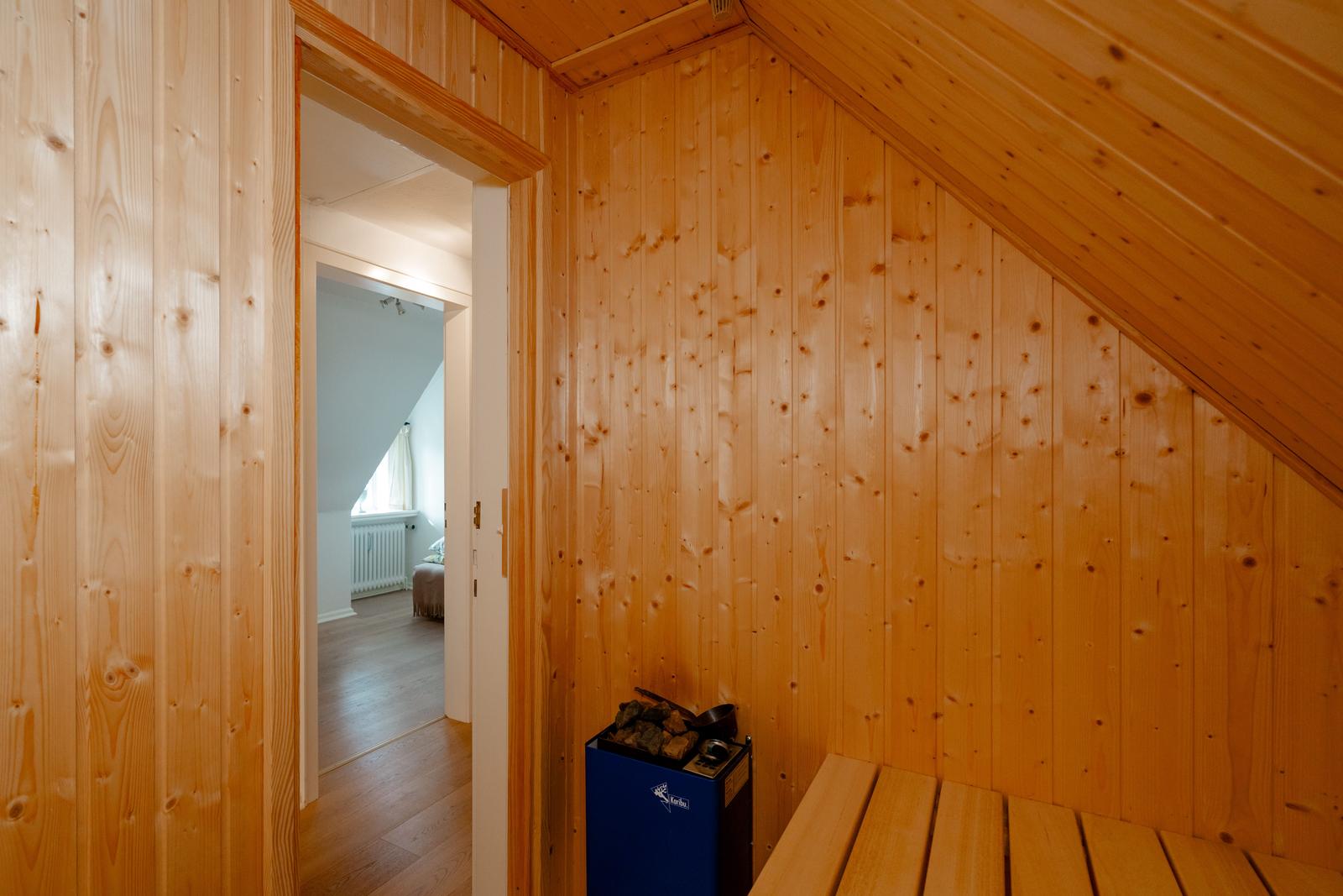 Holzsauna mit Sitzbank und Heizgerät. Durchgang zu einem Schlafzimmer mit Fenster.