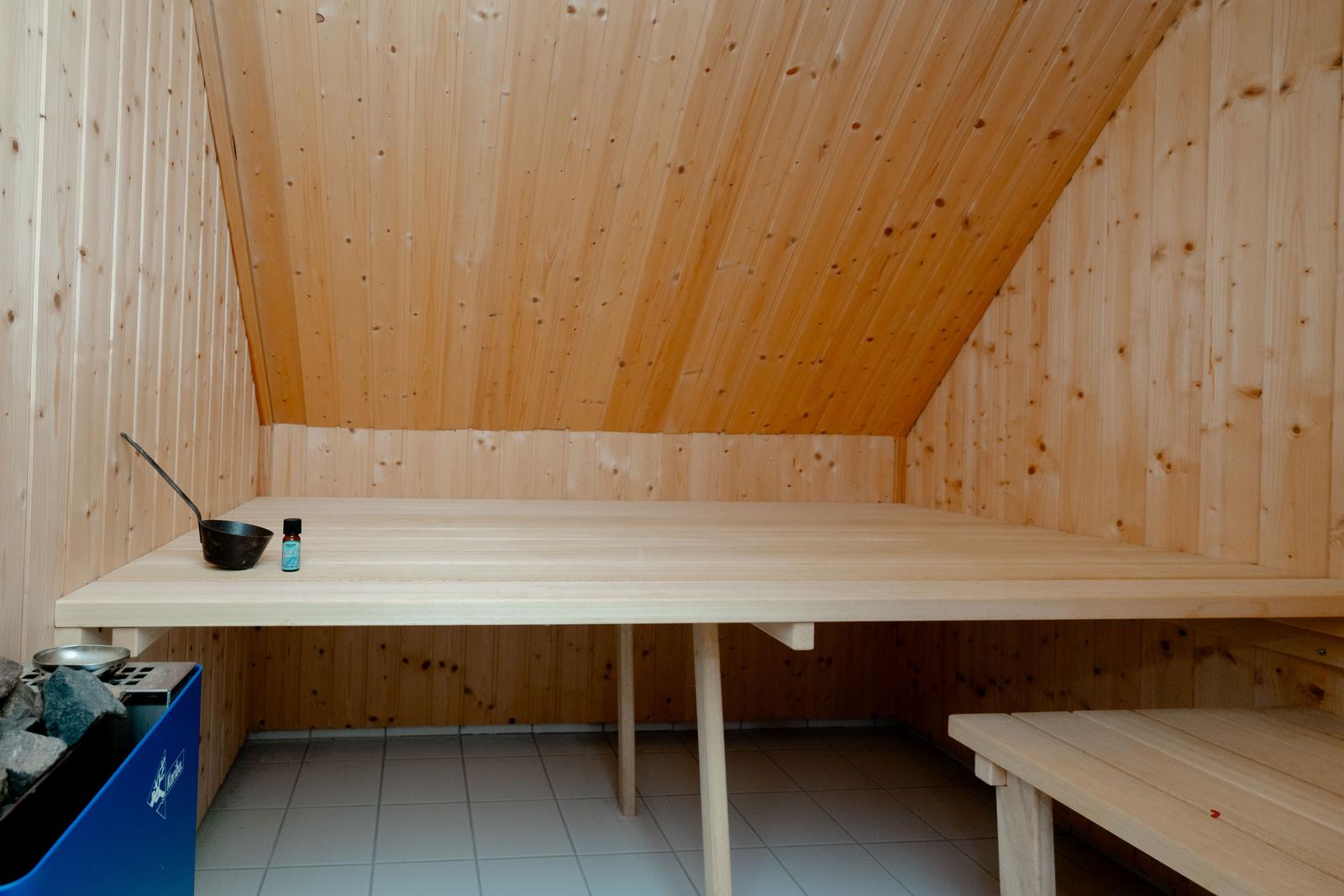 Sauna mit Holzwand und Sitzbank, daneben steht ein kleiner Tisch mit Schale und Flasche.