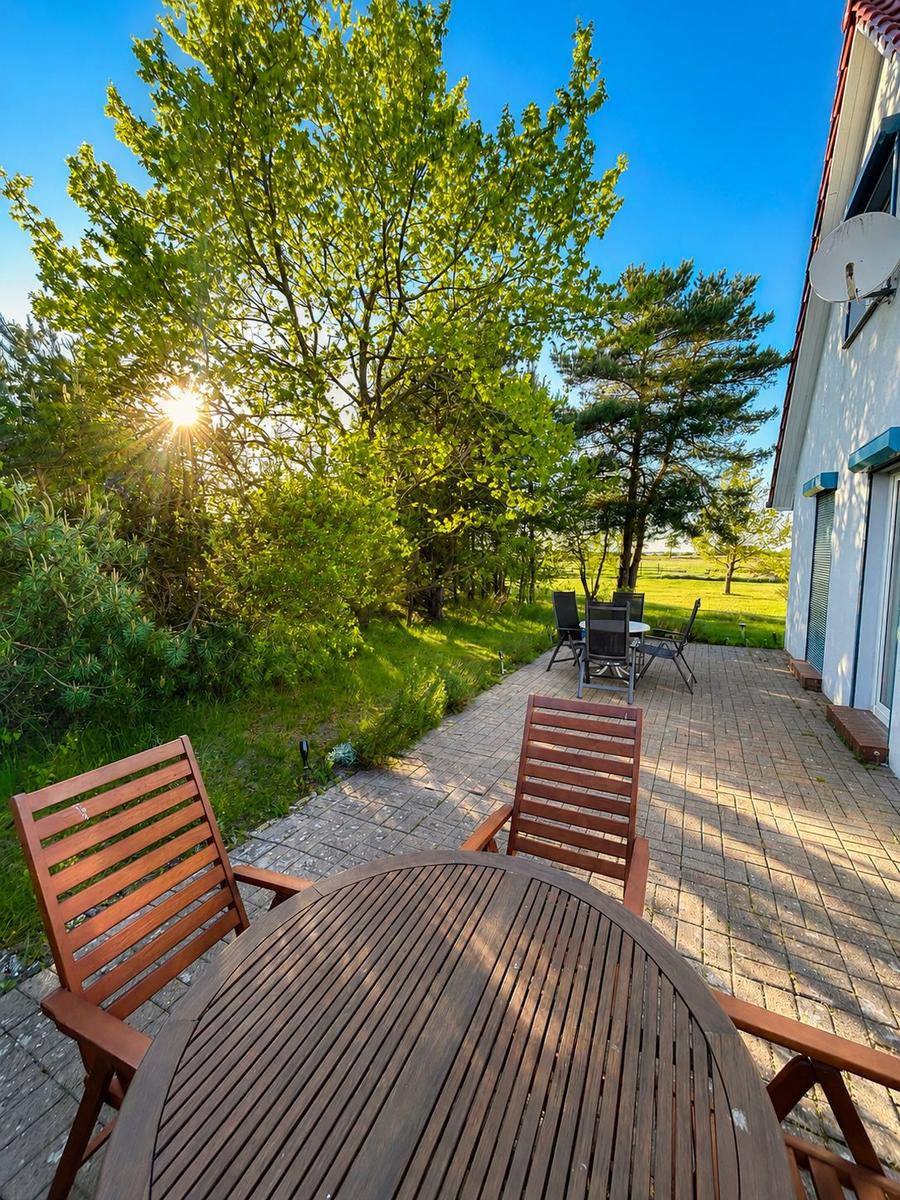 Terrasse mit Holztisch und Stühlen, Blick auf grüne Bäume und einen sonnigen Himmel.