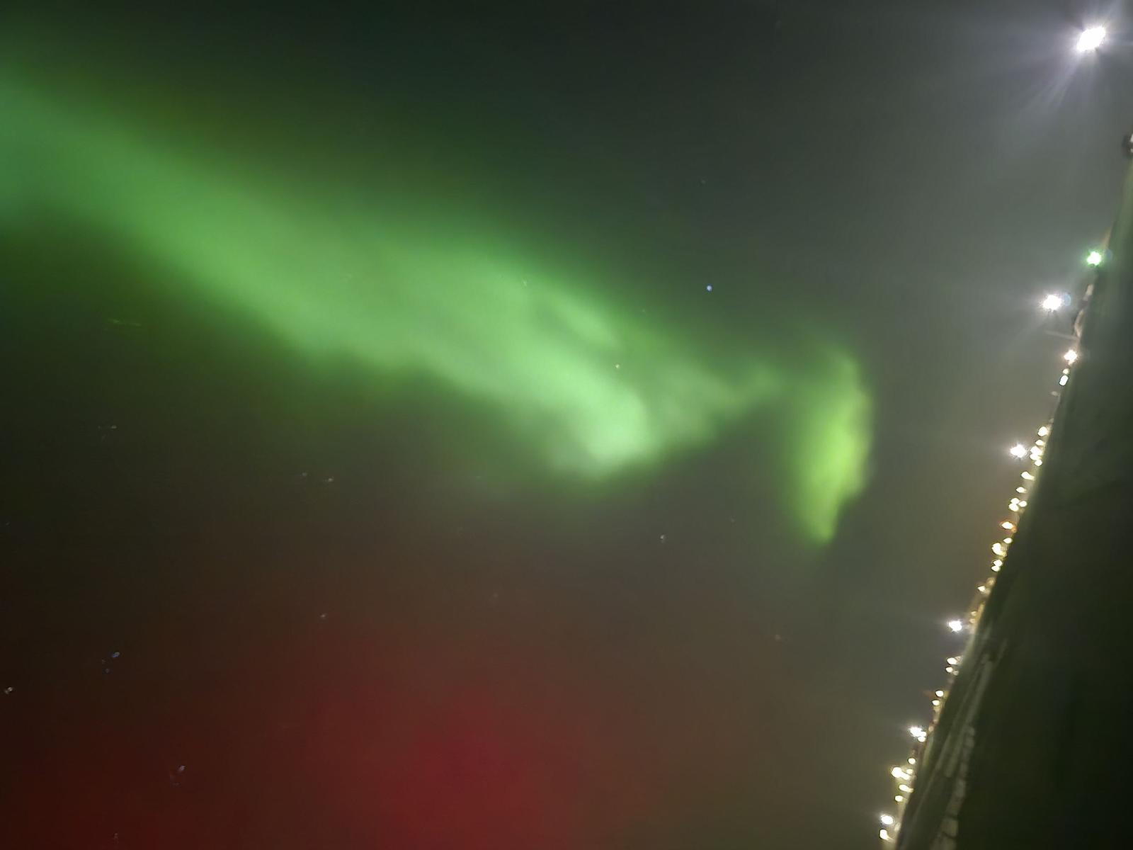 Grüne Nordlichter sind über dem nächtlichen Himmel sichtbar, neben einer beleuchteten Straße.