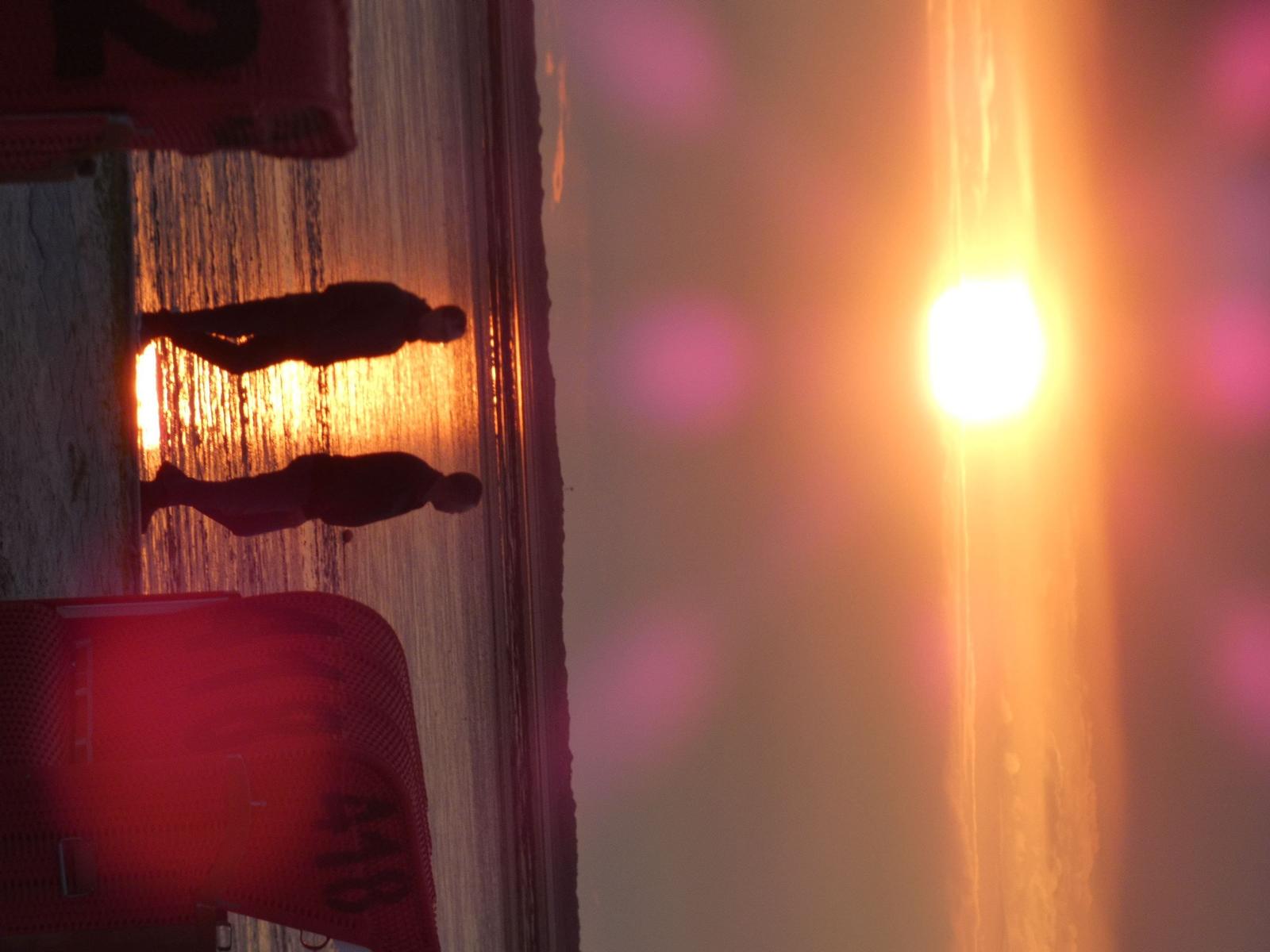 Zwei Personen stehen am Strand bei Sonnenuntergang, das Licht reflektiert auf dem Wasser.