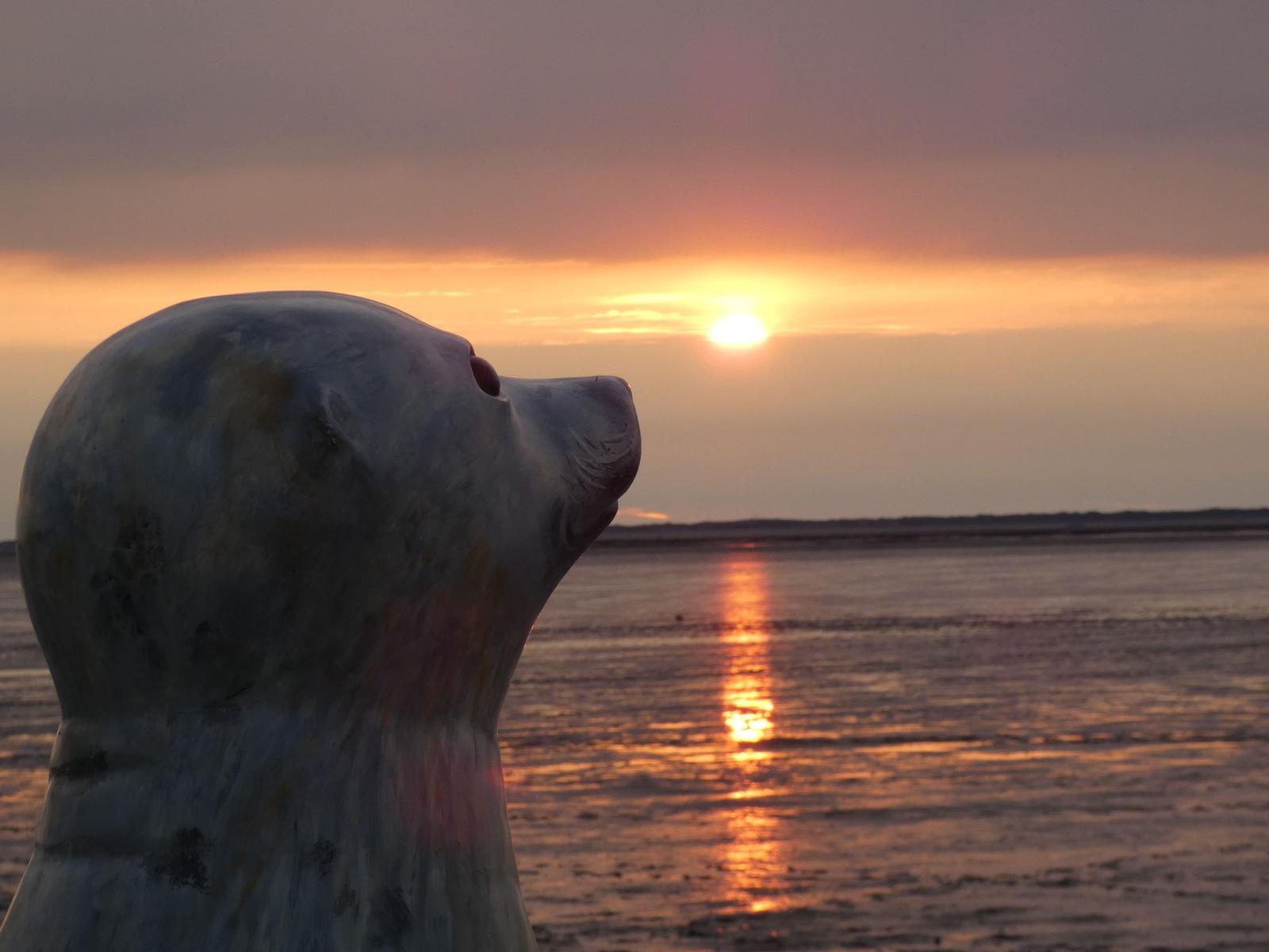 Eine Skulptur blickt auf einen Sonnenuntergang über das Wasser.