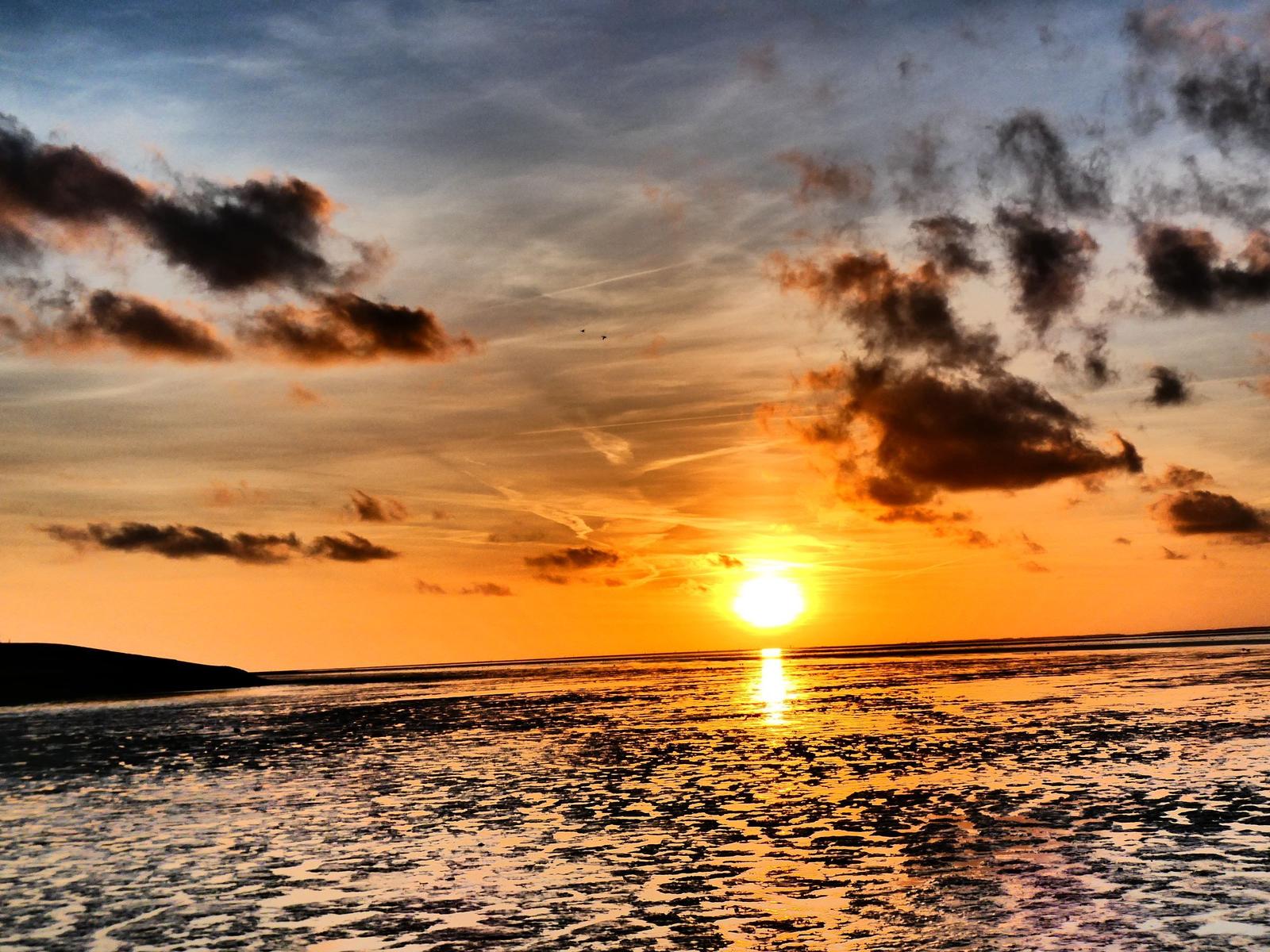 Sonnenuntergang über Wasser mit Wolken und Reflexion.