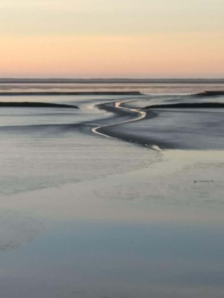 Wasserweg mit flachem Ufer und sanftem Sonnenuntergang am Horizont.