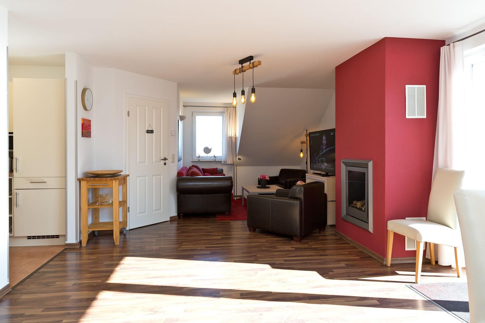 Wohnzimmer mit roter Wand, Kamin, Ledersofa und Holzboden. Küche im Hintergrund.