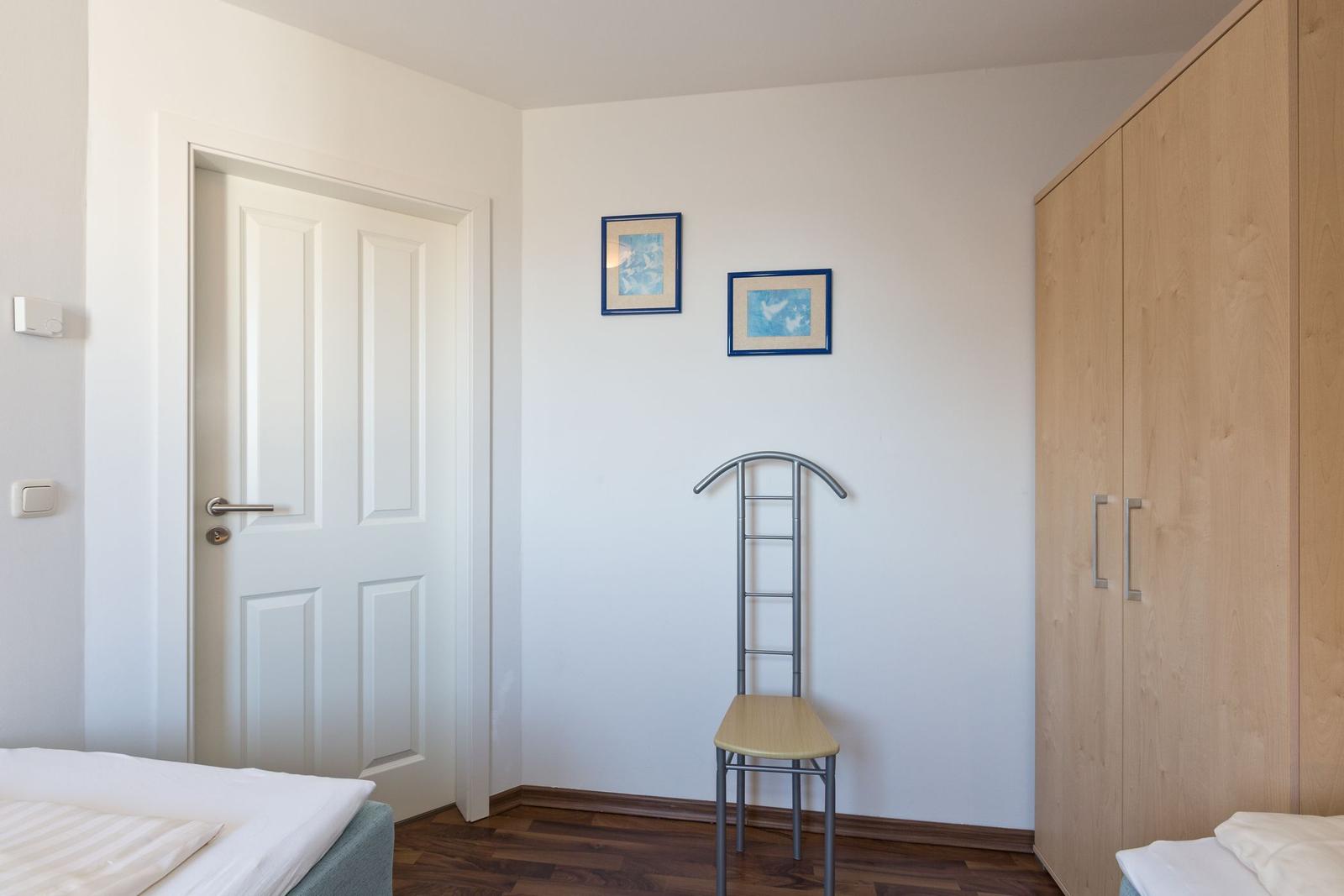 Schlafzimmer mit Bett, Kleiderschrank und Stuhl. An der Wand hängen zwei Bilder.