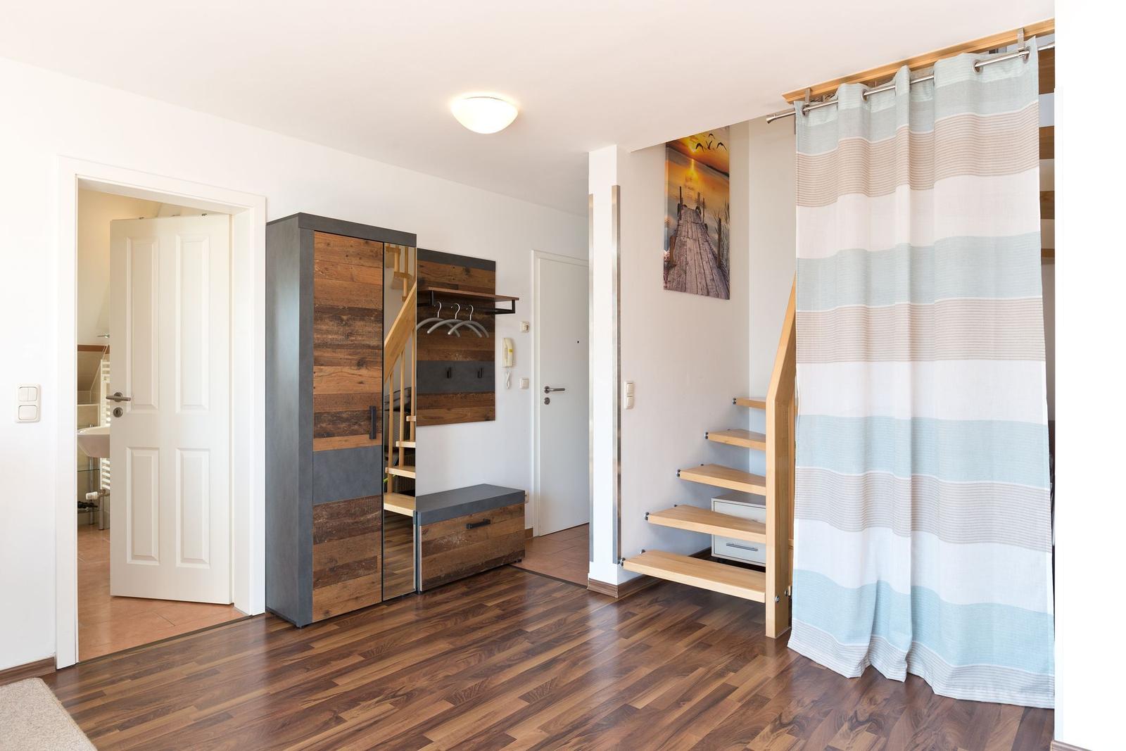 Eingangsbereich mit Kleiderschrank, Treppe und Bad. Holzfußboden und Gardine.