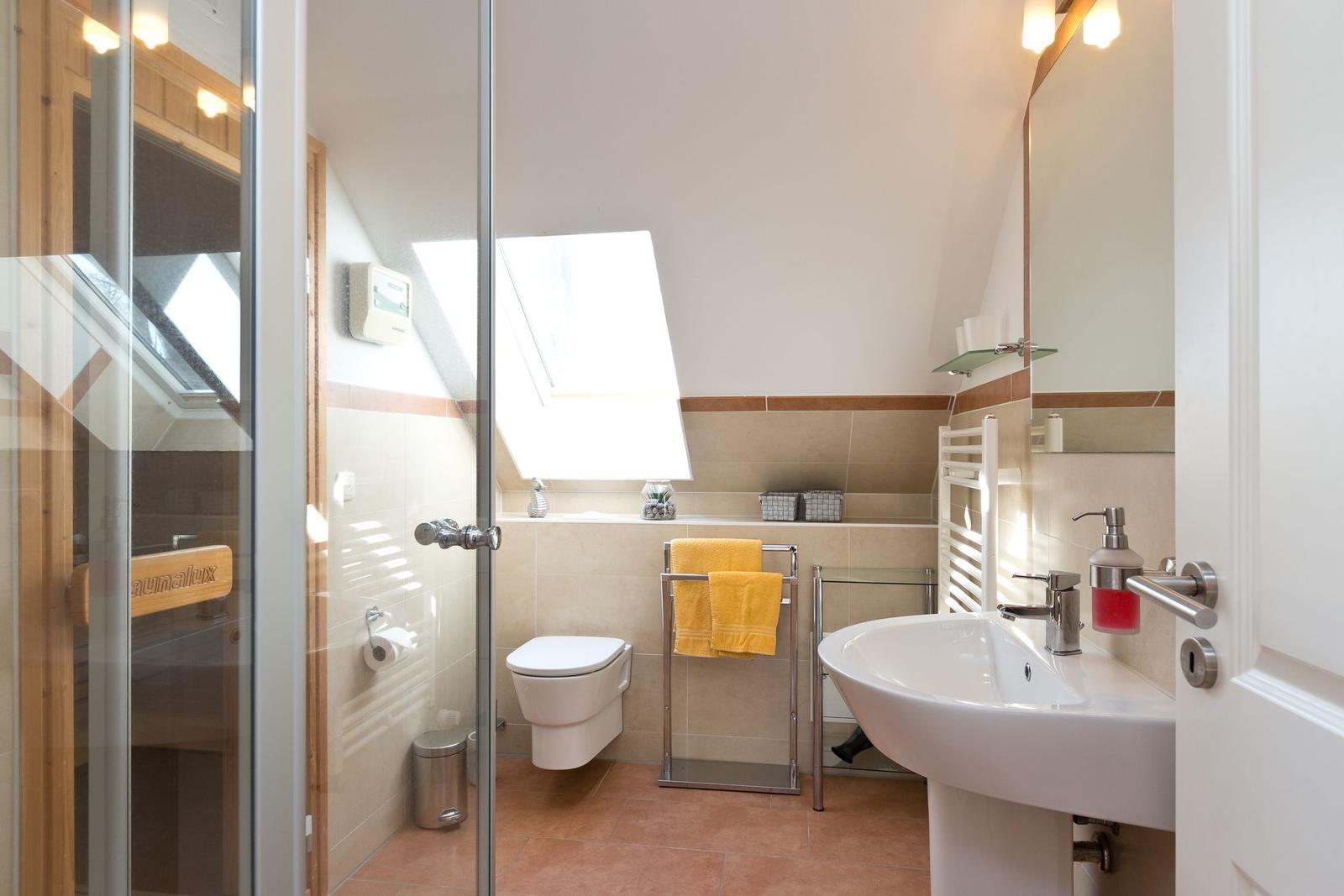 Badezimmer mit Dusche, Toilette und Waschbecken unter Dachschrägen.
