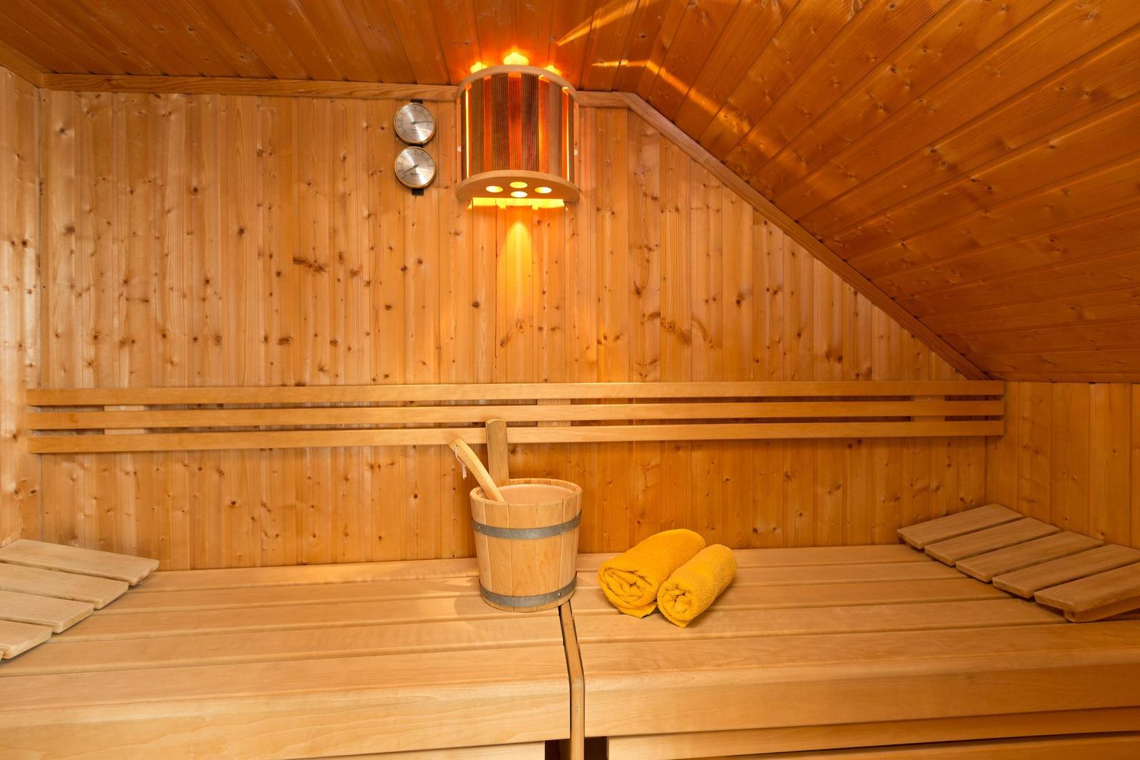 Sauna mit Holzbank, Eimer und gelben Handtüchern. Decke und Wände aus Holz.