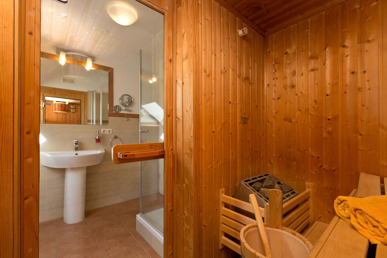 Sauna mit Holzbank und Eimer. Nebenraum mit Dusche und Waschbecken.