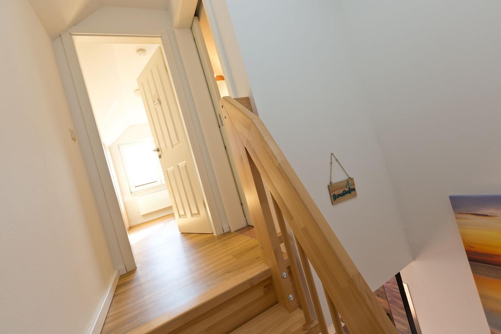 Holzgetreppe mit Handlauf führt zu einem Raum mit Holzboden und weißer Tür.