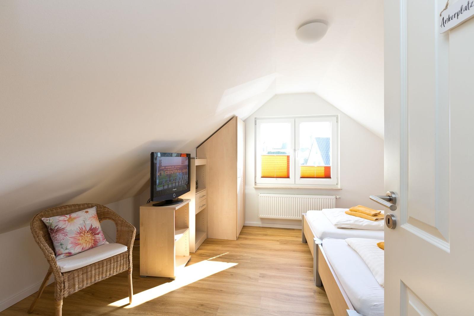 Zimmer mit zwei Betten, TV und Sitzgelegenheit unter Dachschräge.