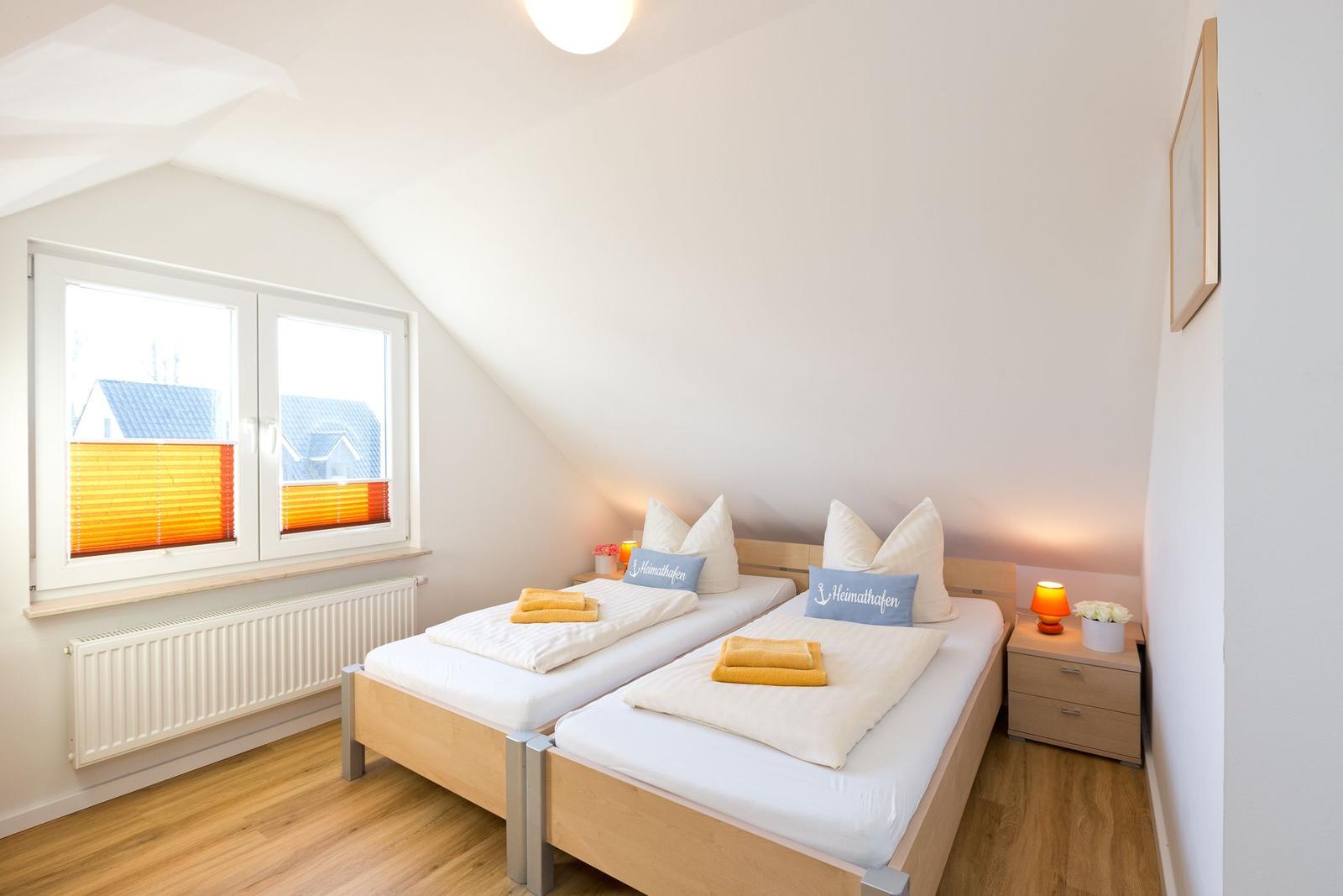 Zimmer mit zwei Betten, Fenster und Nachttisch.
