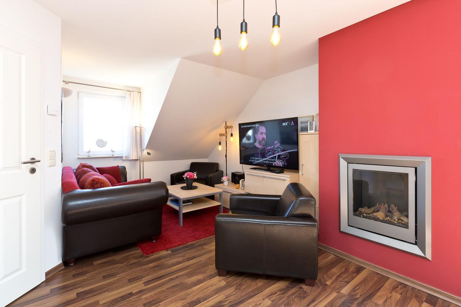 Wohnzimmer mit roter Wand, Kamin, Sofa und Fernseher.