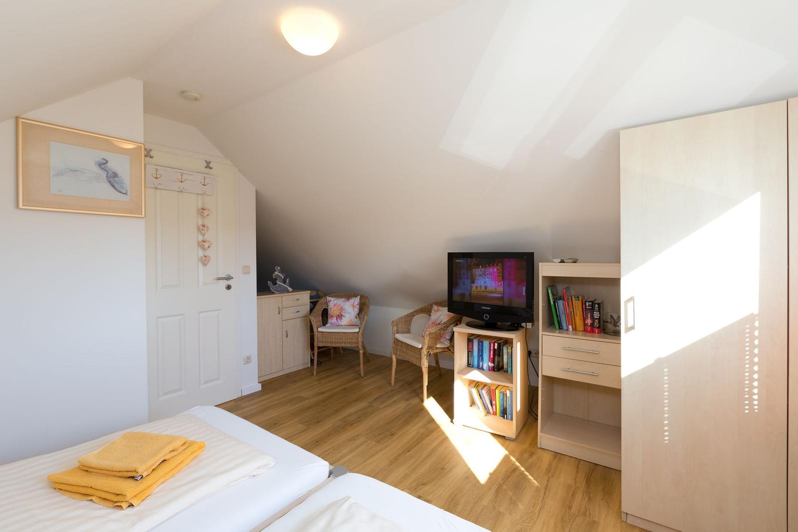 Schlafzimmer mit Dachschrägen, Bett, Fernseher und Schränken.
