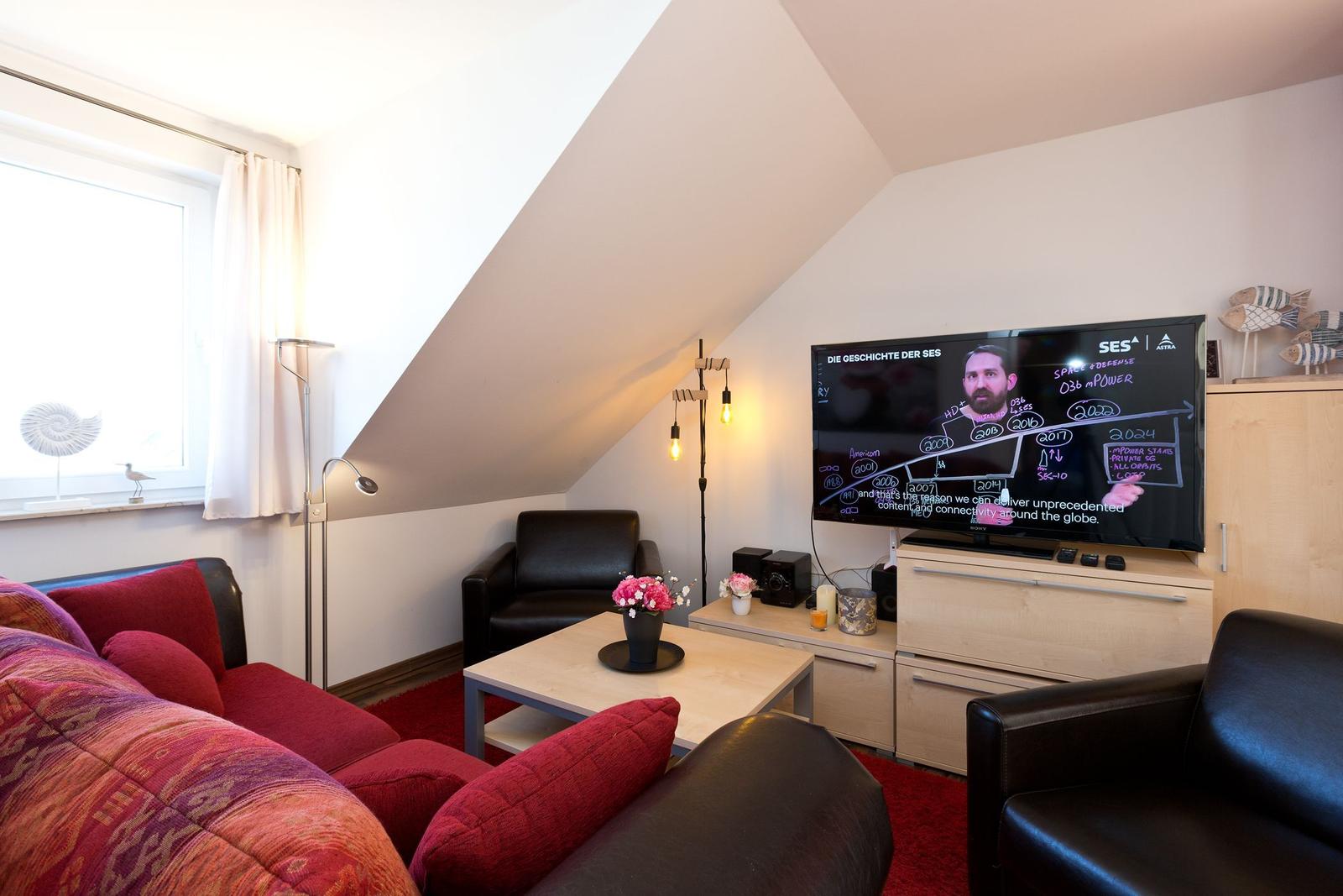 Wohnzimmer mit Sofa, Sessel und Fernseher unter Dachschräge