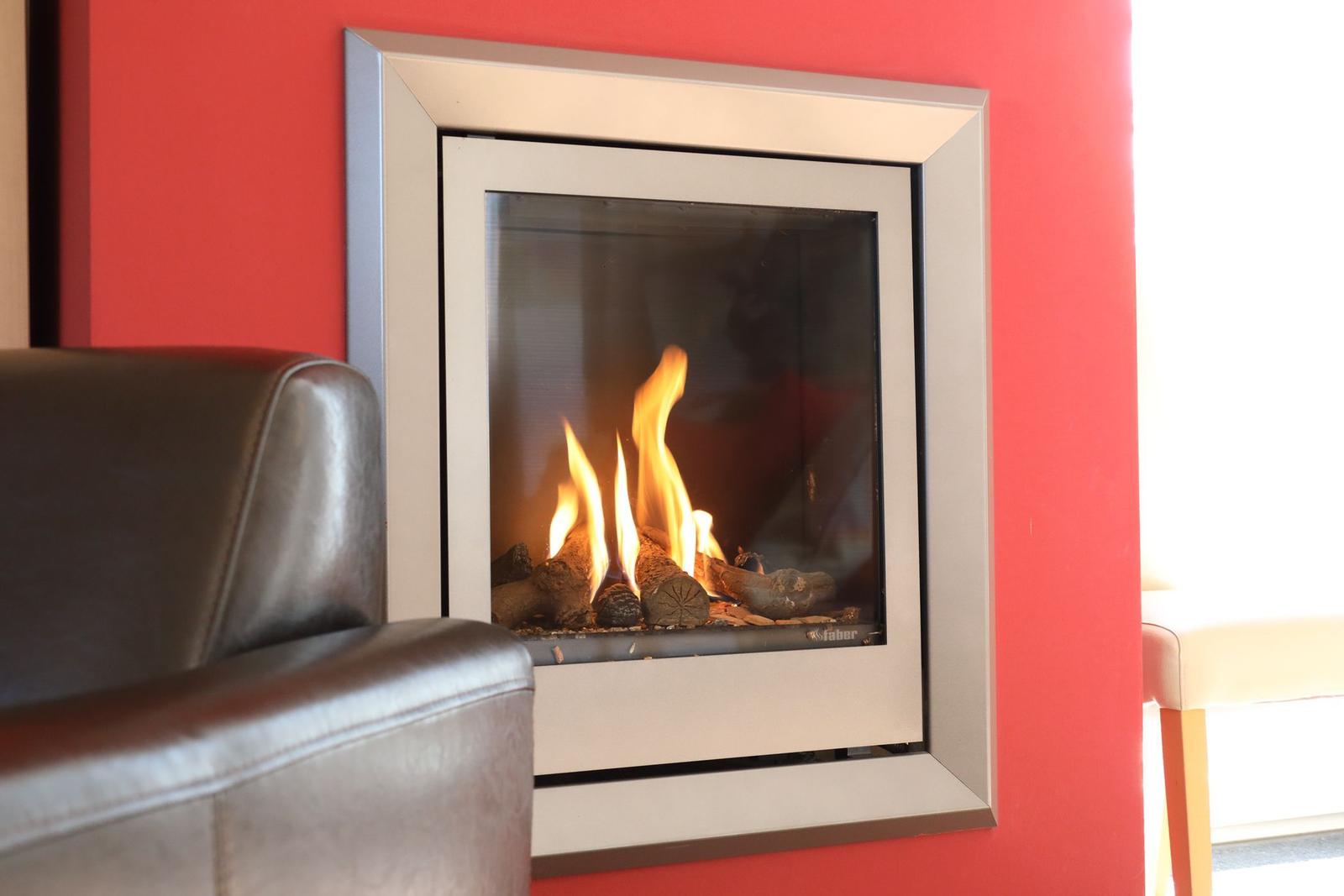 Ein moderner Kamin mit brennenden Holzscheiten an einer roten Wand.