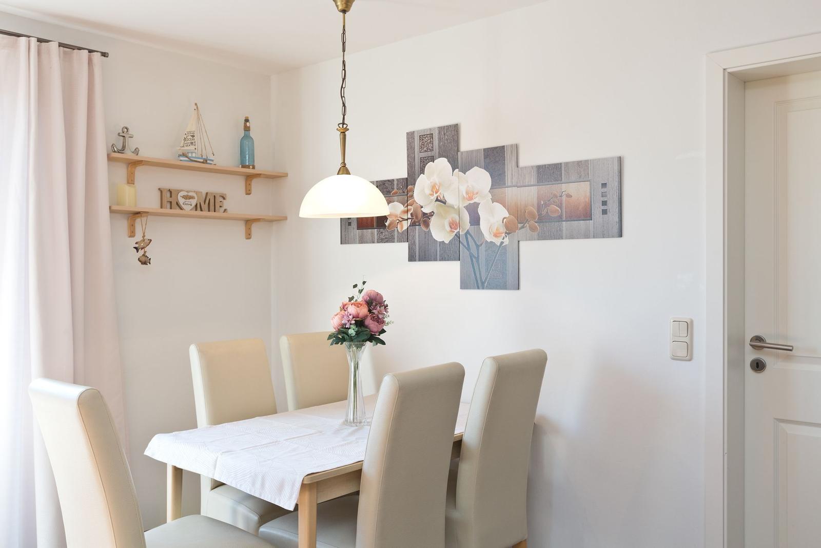 Esszimmer mit Tisch, Stühlen, Wandbild und Deckenleuchte. An der Wand hängt ein Bild mit Orchideen.