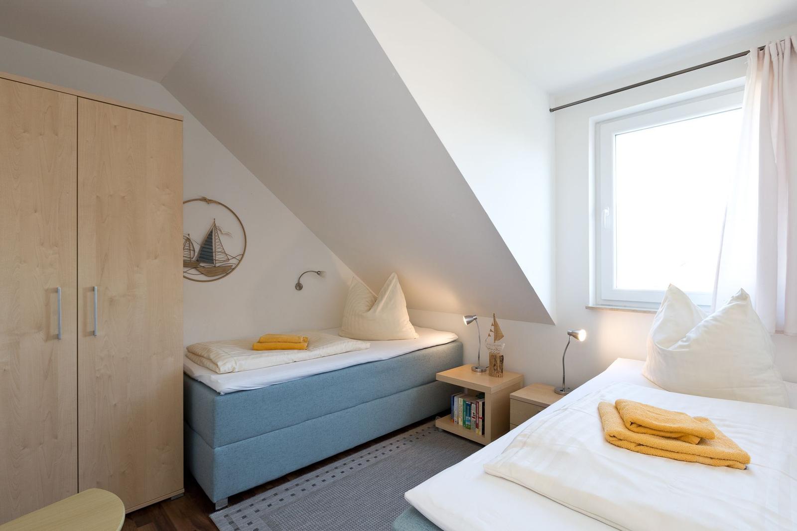 Zimmer mit zwei Betten, Schrank und Fenster unter Dachschrägen.