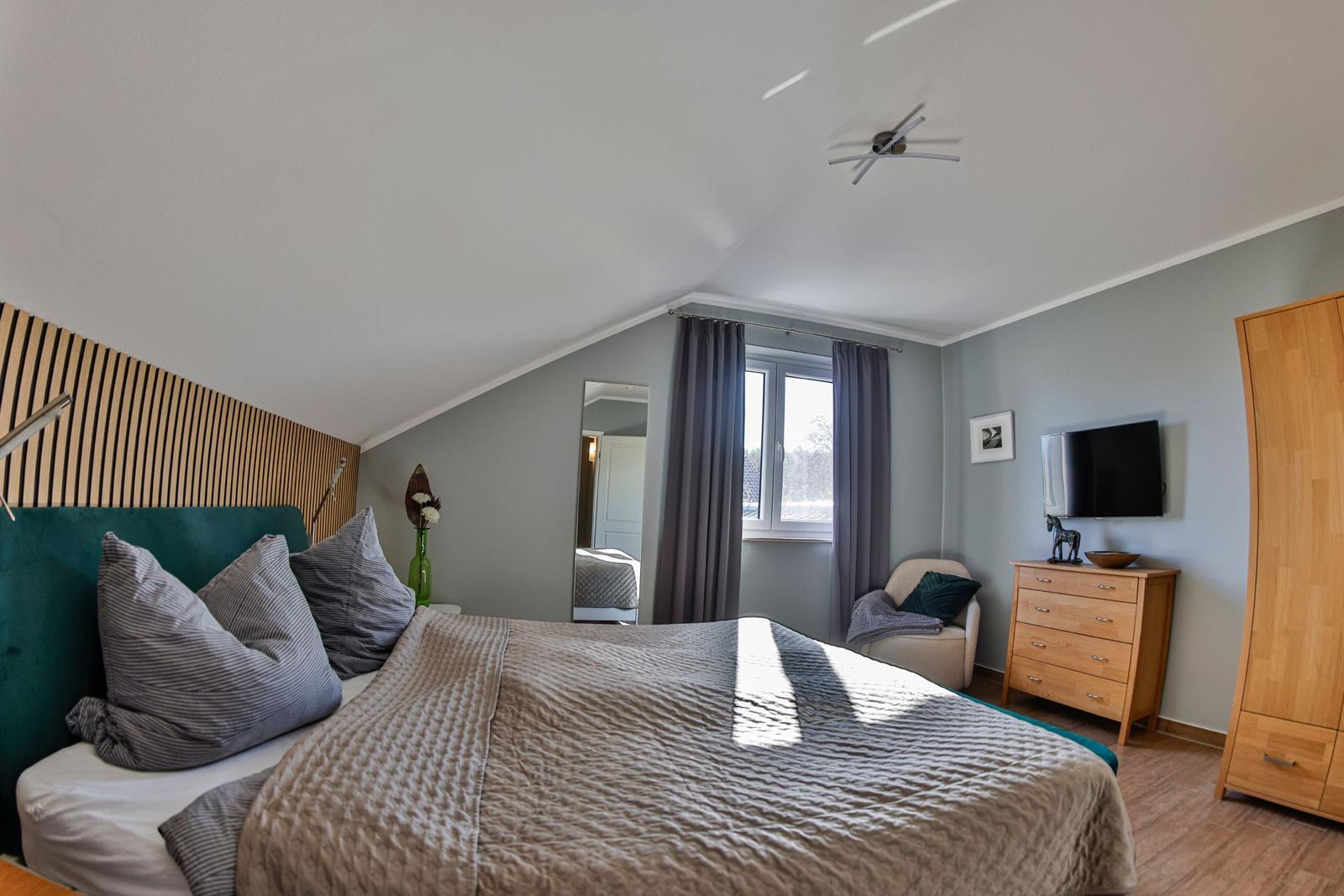 Schlafzimmer mit Bett, Kleiderschrank und TV. Fenster mit Vorhängen und Spiegel.