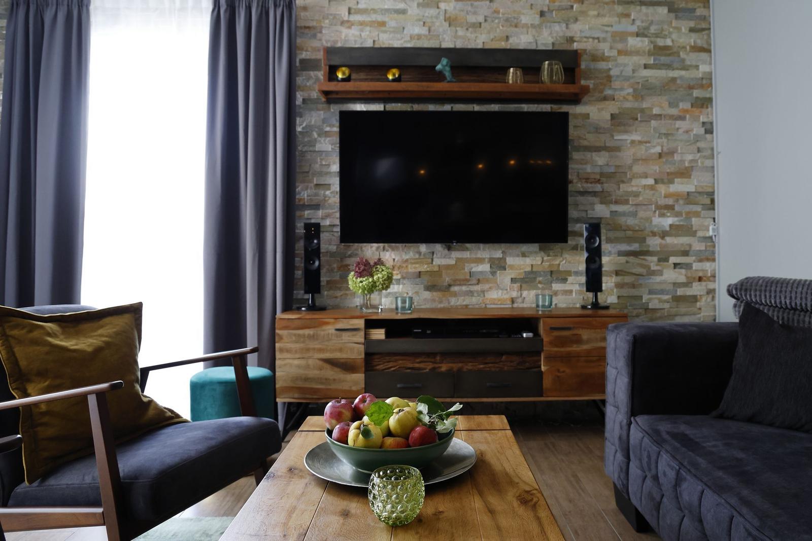 Wohnzimmer mit Fernseher, Holztisch und Steinwand