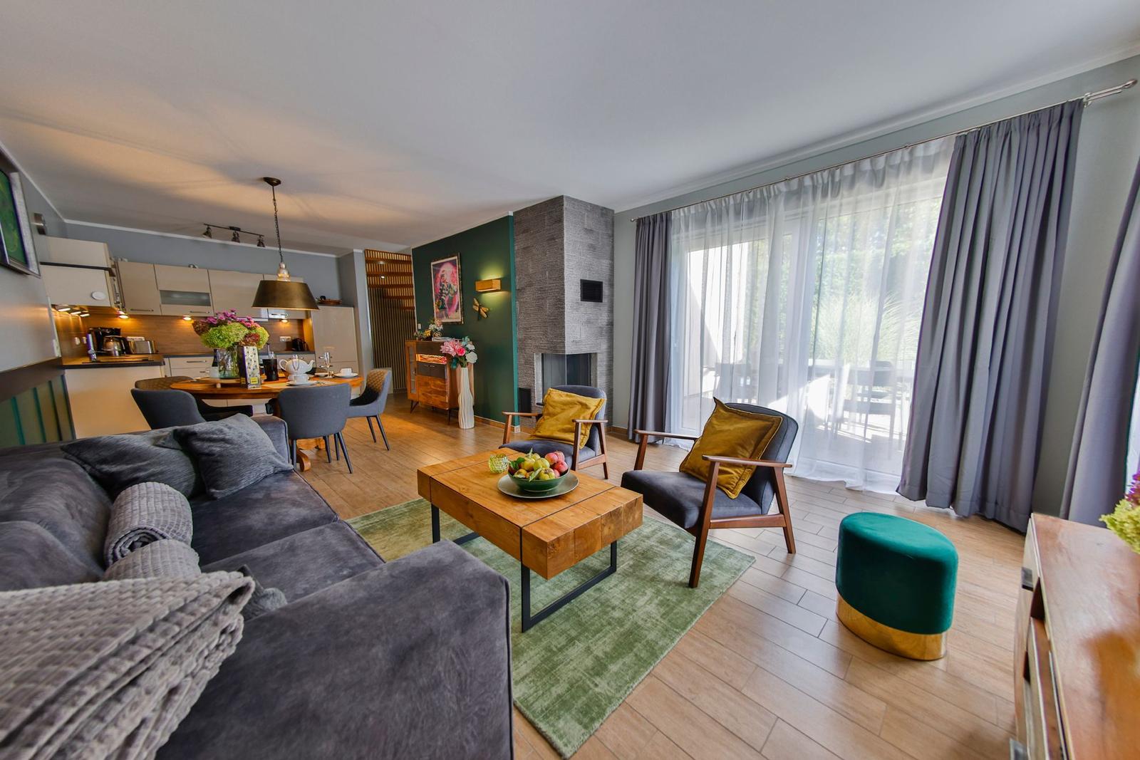 Wohnbereich mit Sofa, Sesseln und Kamin. Durchgang zur Küche und Terrasse.