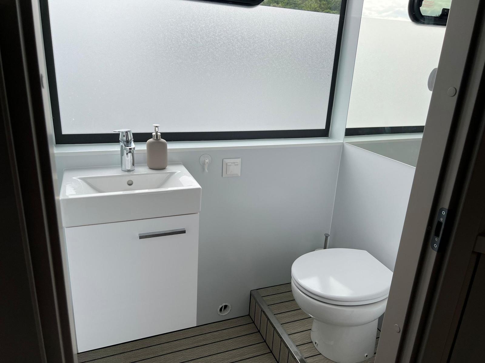 Badezimmer mit Waschbecken, Toilette und großem Fenster.
