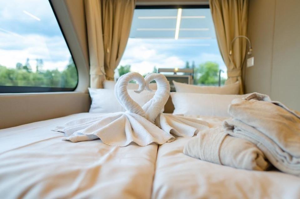 Zwei Handtücher in Form von Schwänen auf dem Bett. Durchgehendes Fenster mit Blick auf Grün.