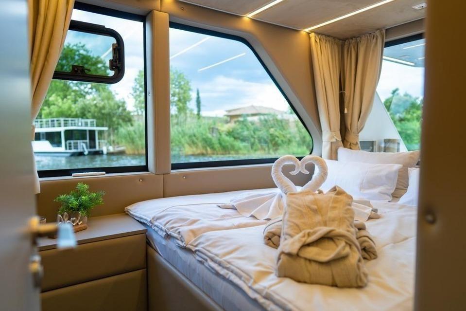 Schlafzimmer mit Blick auf Wasser und Ufervegetation. Bett mit Handtuchschwanen.